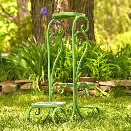 two green metal plant stands sitting in the grass next to a tree and flower bed