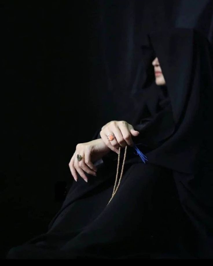 a woman wearing a black veil and holding a blue string in her hand with both hands