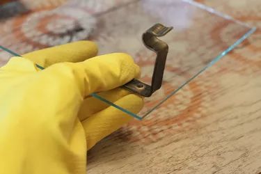 a person wearing yellow gloves is holding a piece of glass with a metal object on it