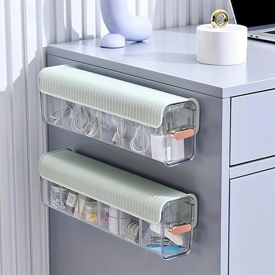 two clear plastic containers are attached to the side of a gray desk with white drawers