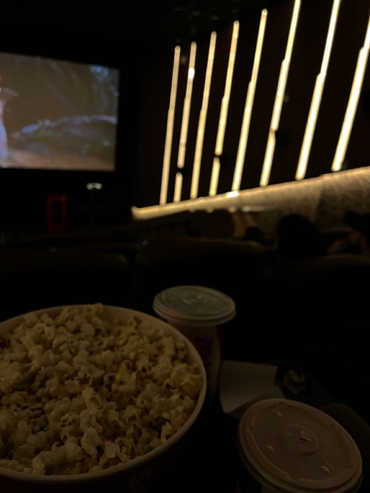 a bowl of popcorn and two cups of soda on a table in front of a screen