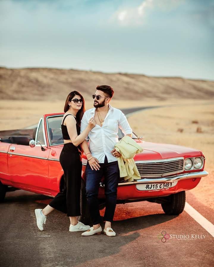 a man and woman standing next to a red car