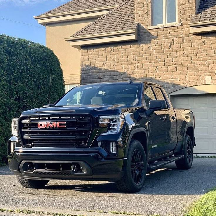 a black gmc truck parked in front of a house next to a garage door