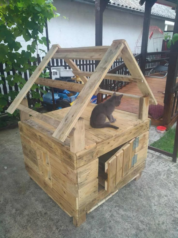 a cat house made out of pallet wood with a cat sitting on the roof