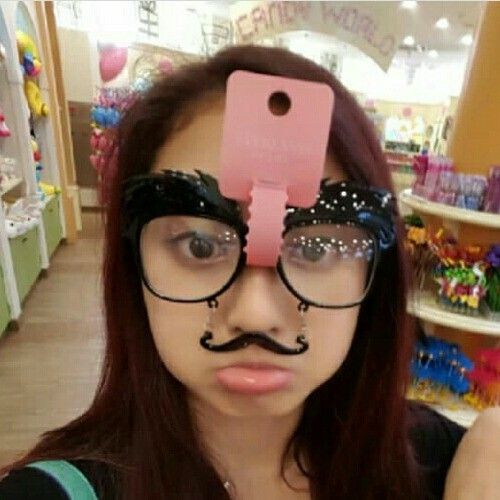 a woman with glasses and a fake mustache on her head is taking a selfie