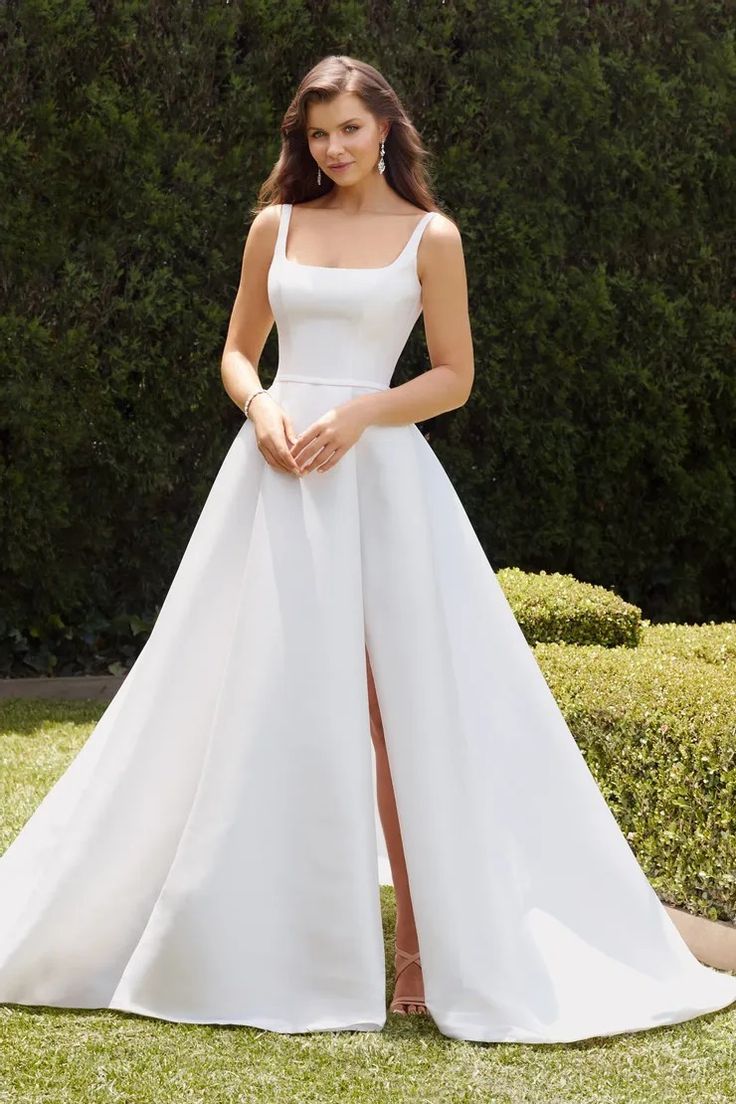 a woman in a white wedding dress standing on the grass with her legs crossed and looking at the camera