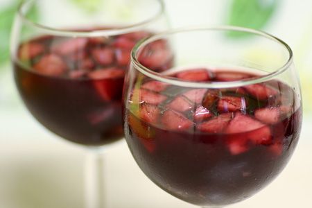 two glasses filled with red wine and strawberries on top of a table next to each other