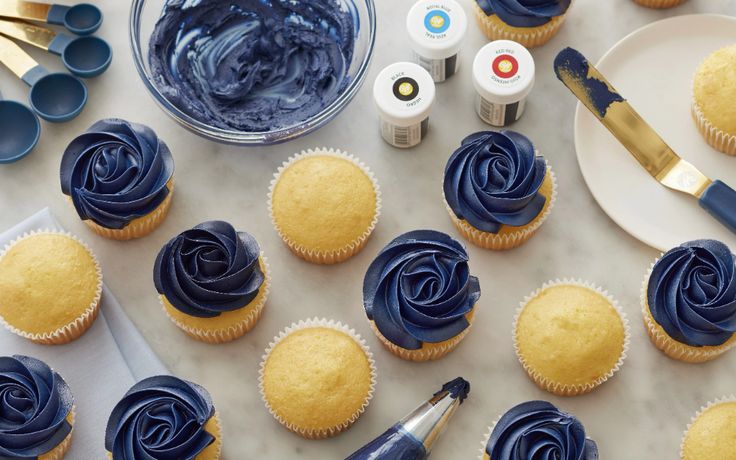 cupcakes with blue icing and yellow frosting are on the table next to some paintbrushes