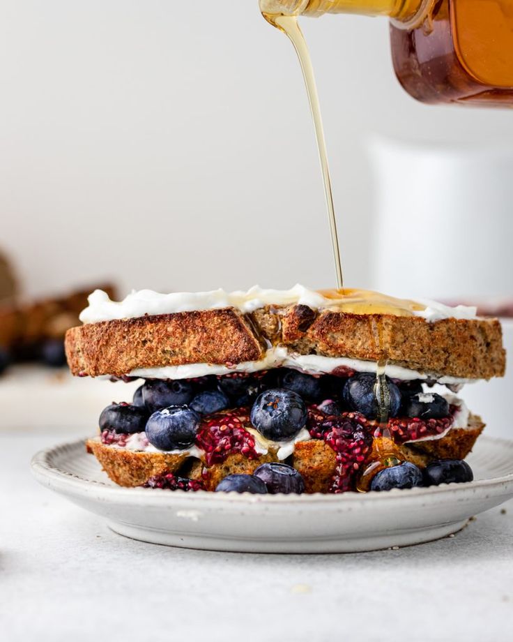 a sandwich with blueberries, strawberries and honey being drizzled on it