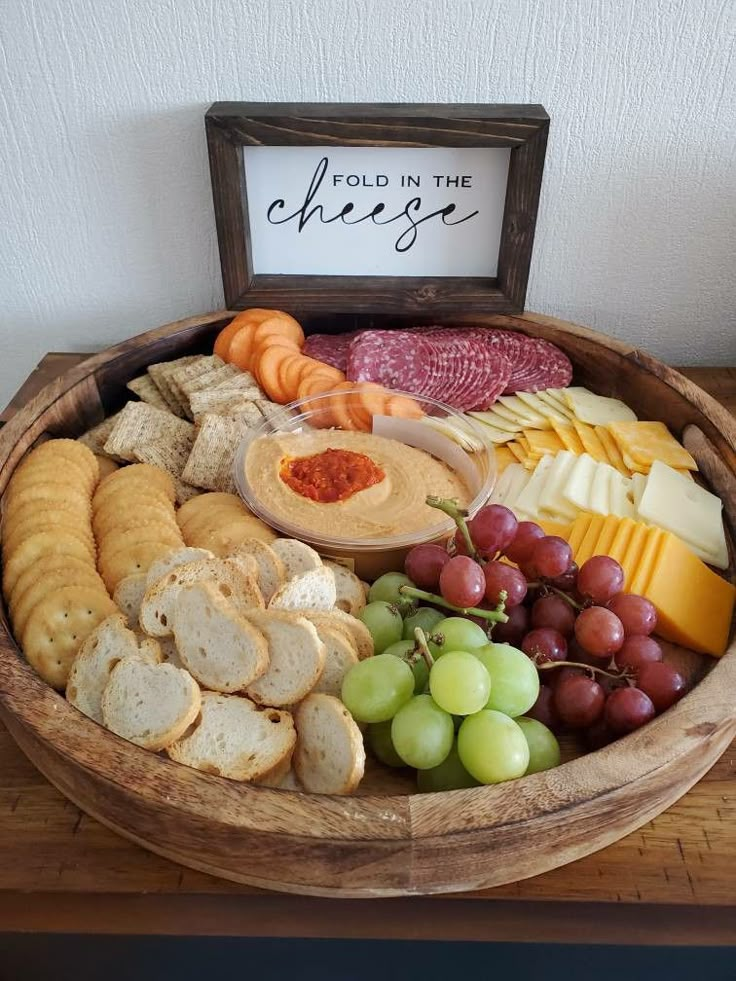 a wooden bowl filled with cheese, crackers and grapes