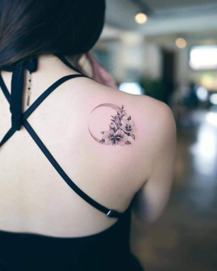 the back of a woman's shoulder with a flower and crescent tattoo on it