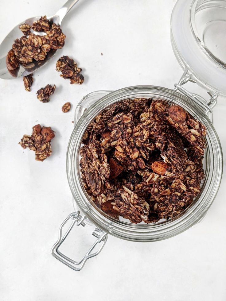 a glass jar filled with granola on top of a white counter next to a spoon