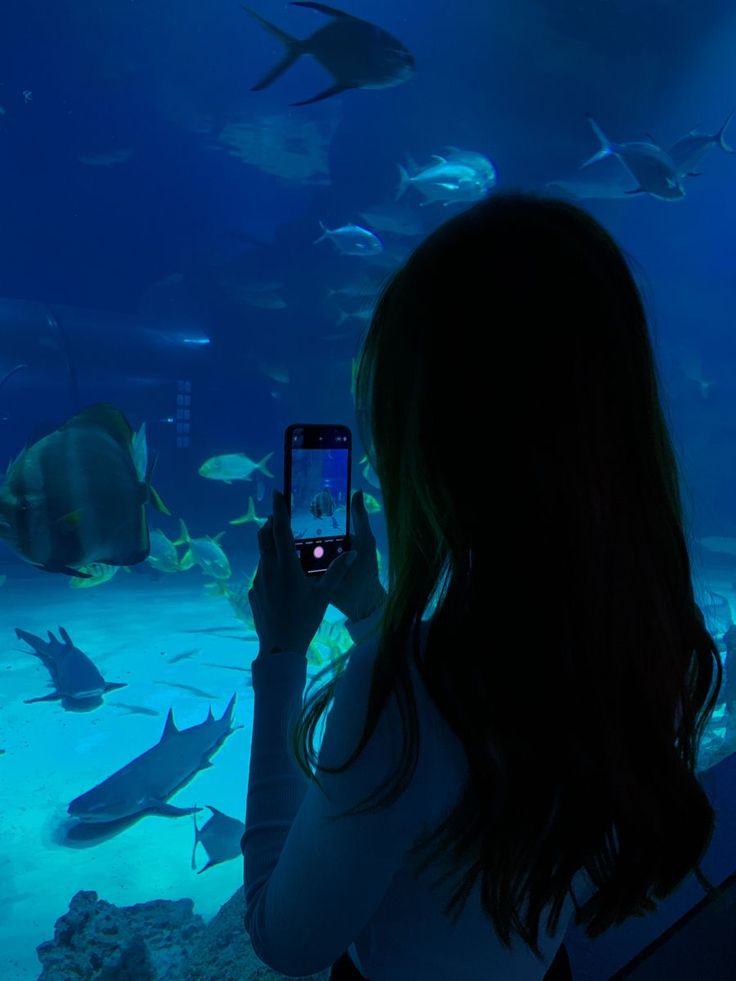 a woman taking a photo of fish in an aquarium with her cell phone at night