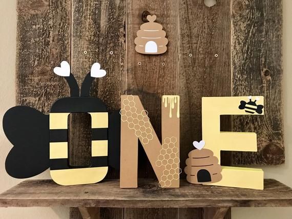 a wooden sign that says one with bees and honeycombs on the letters, sitting on a shelf