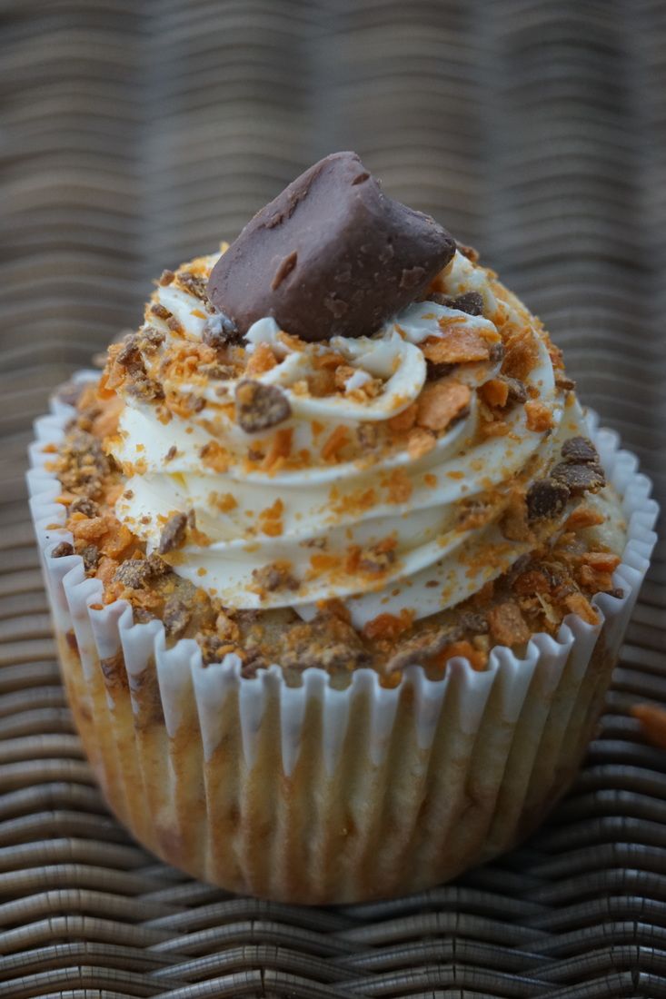 a cupcake with white frosting and chocolate on top sitting on a wicker table