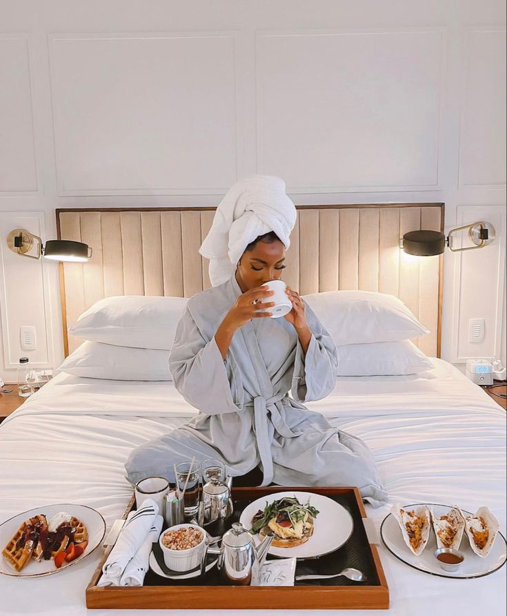 a woman sitting on top of a bed holding a coffee cup in front of her face