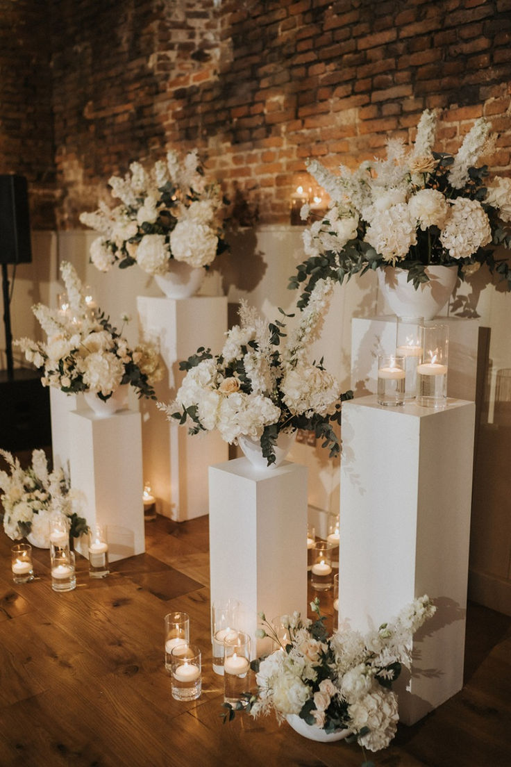 several tall white vases with flowers and candles