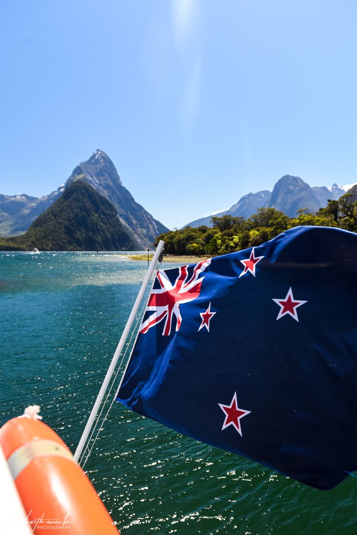 an australian flag flying from the back of a boat on water with mountains in the background