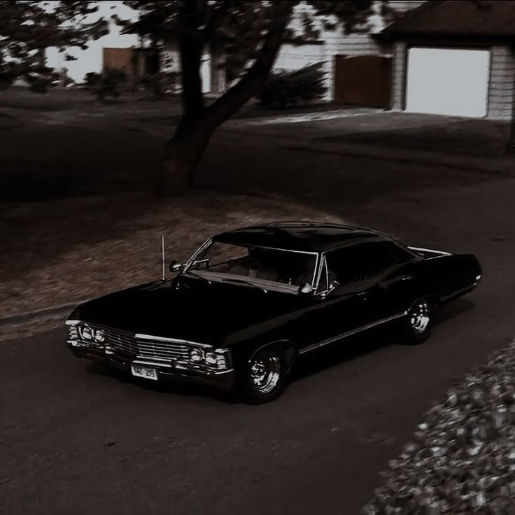 an old black car is parked on the side of the road in front of a house