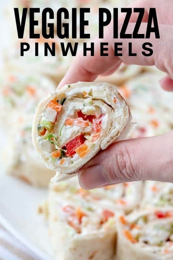 a hand holding a vegetable wrap over a white plate