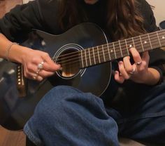 a woman sitting on the floor playing an acoustic guitar with her hands and fingers together