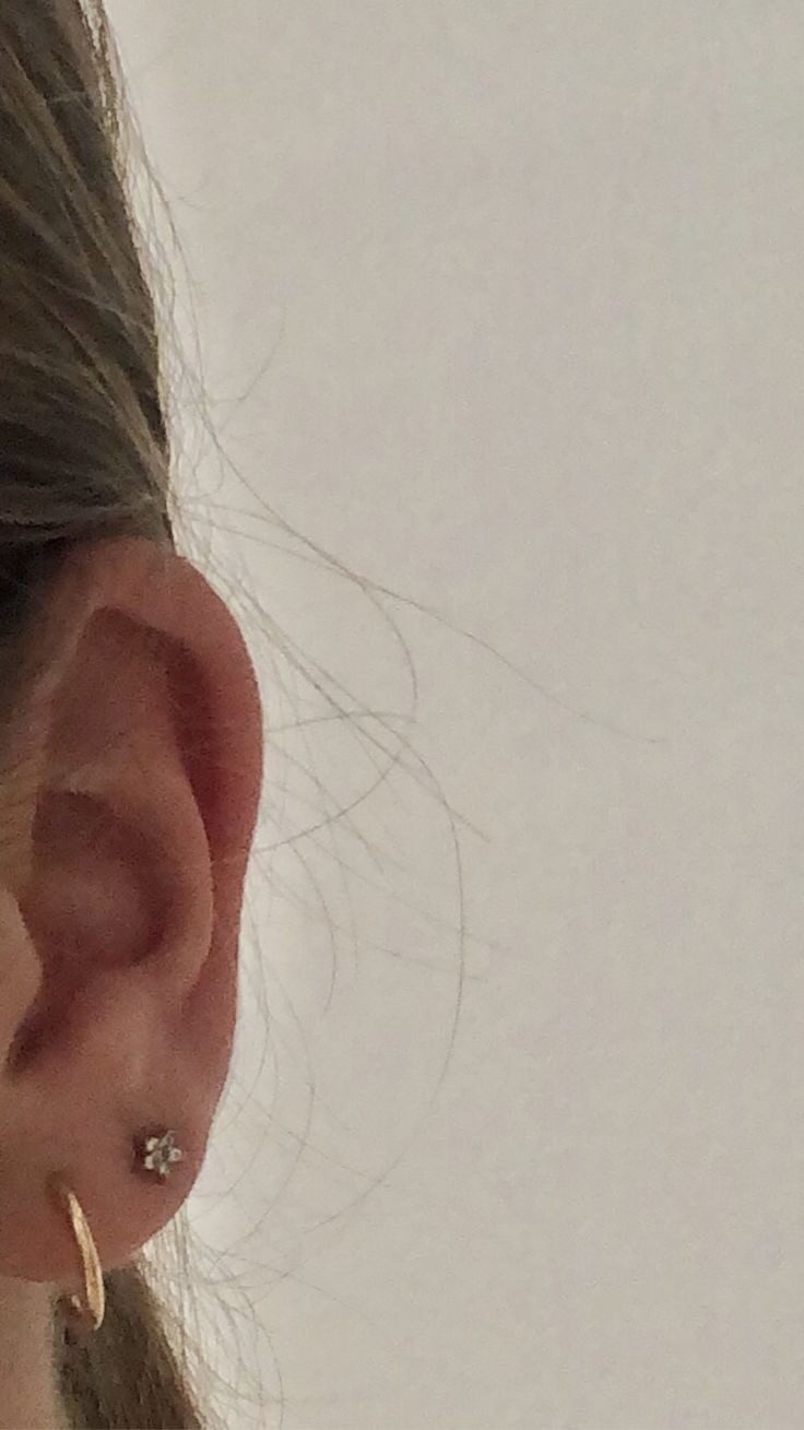 a close up of a person's ear wearing gold hoop earrings and a white background