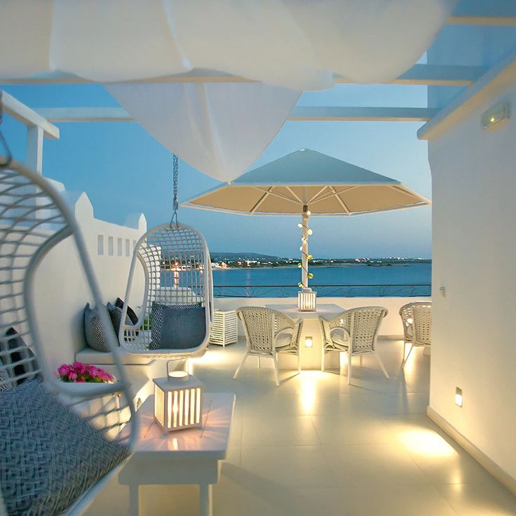 an outdoor seating area with chairs and umbrellas overlooking the ocean at dusk or dawn