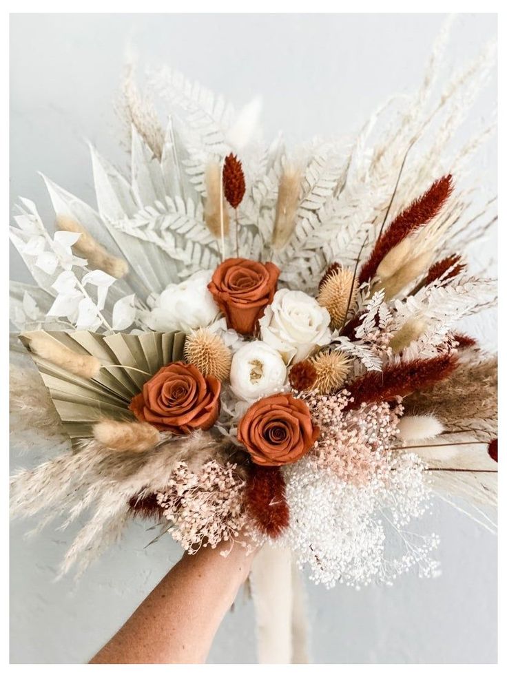 a hand holding a bouquet with flowers and feathers