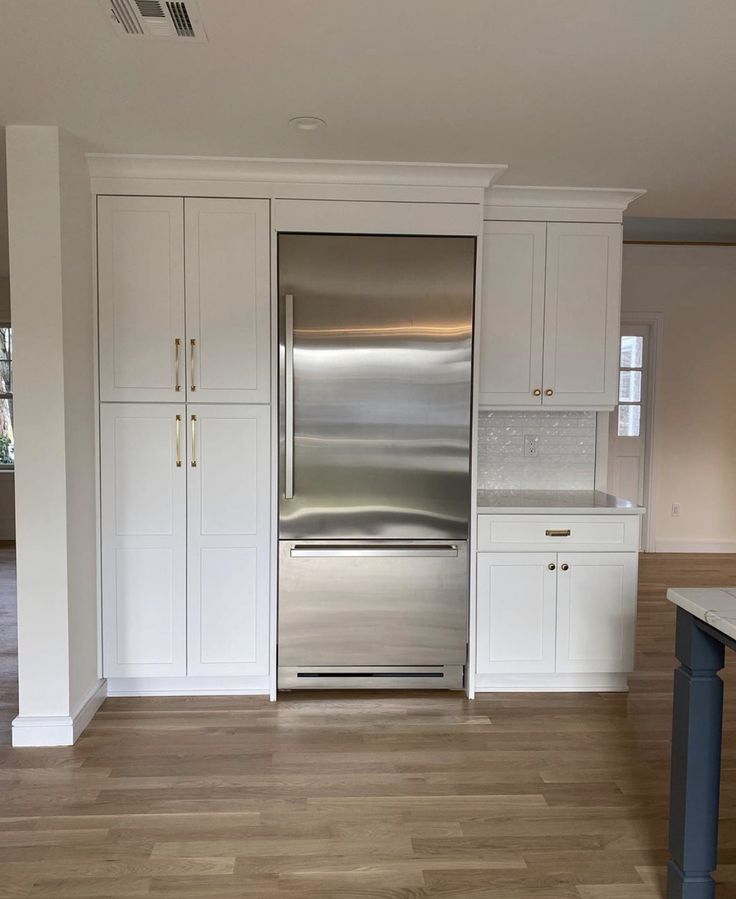 an empty kitchen with white cabinets and stainless steel refrigerator in the center, on hard wood flooring