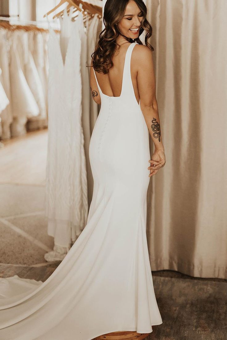 a woman in a white dress standing next to a rack of wedding gowns and dresses