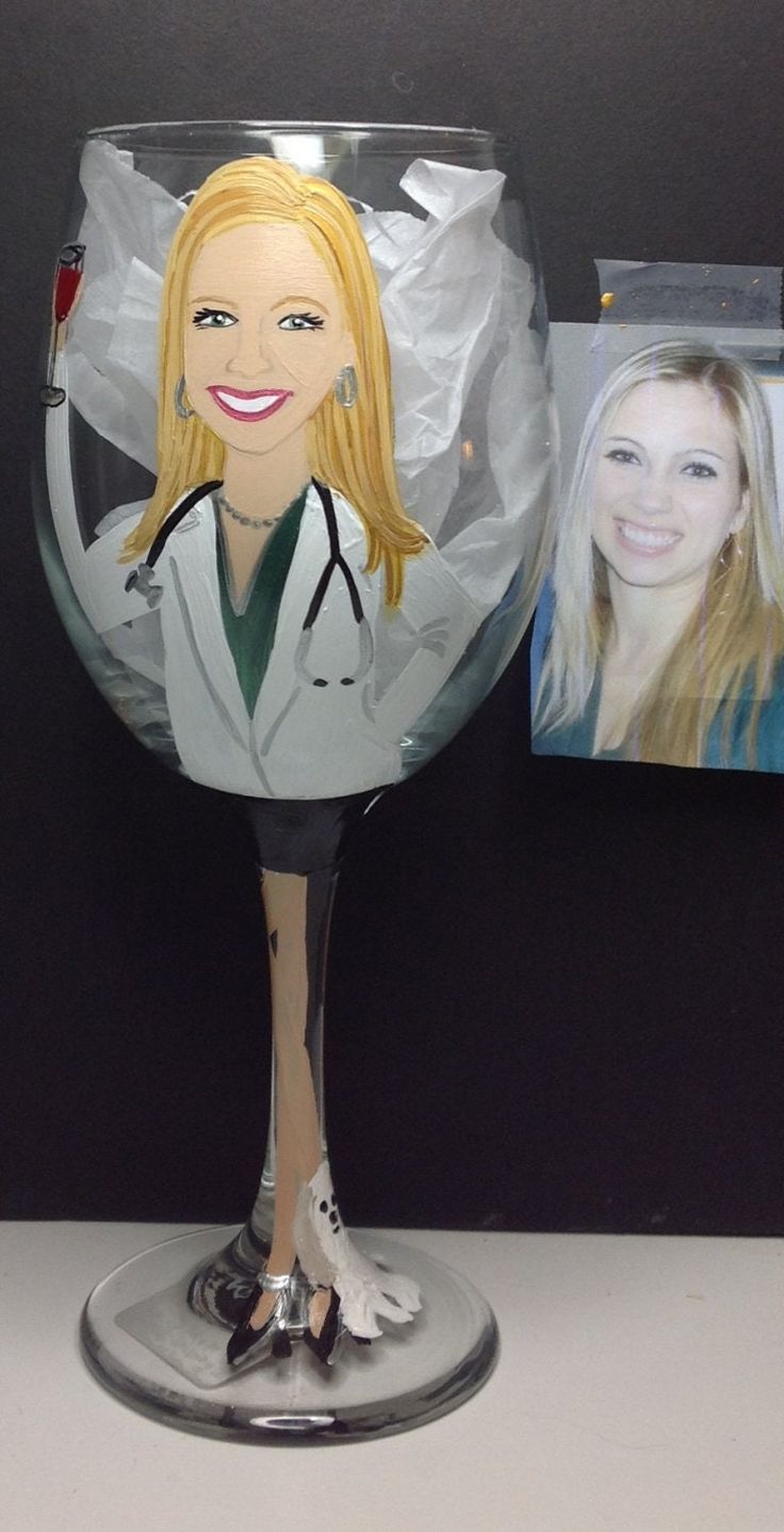 a wine glass with a woman's face painted on the side and two pictures behind it