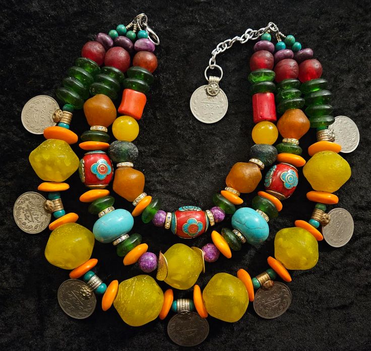 This is a big, bold, chunky, heavy and showy piece, designed for unisex but probably more comfortable worn on a male. Adjusting from 16-20", this closes with silver tone hardware, a lobster claw clasp, 4" extender chain and a Kuchi coin suspended from the end. The components include African yellow recycled glass beads (they do have imperfections), vintage Kuchi coins, orange zebu bone disks, green magnesite round spacers, green recycled glass rondelles, ruby red glass rounds, purple jade, red coral nuggets, blue African glass, rhinestone rondelles, orange African recycled glass, fancy red Tibetan inlaid tribal beads and yellow jade. This is a statement piece to turn to when you want attention and need to add color to an outfit. Much more striking live than the photographs depict. From the Heavy Bohemian Multicolor Necklaces, Bohemian Heavy Multicolor Necklaces, Bohemian Multicolor Necklaces, Yellow Jade, Recycled Glass Bead, Purple Jade, Bold Jewelry, Unisex Necklace, Red Coral