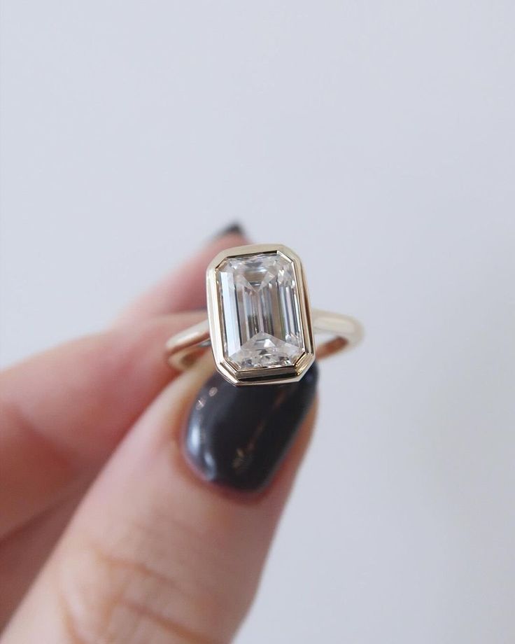 a woman's hand holding a ring with an emerald stone in the middle and a diamond on the side