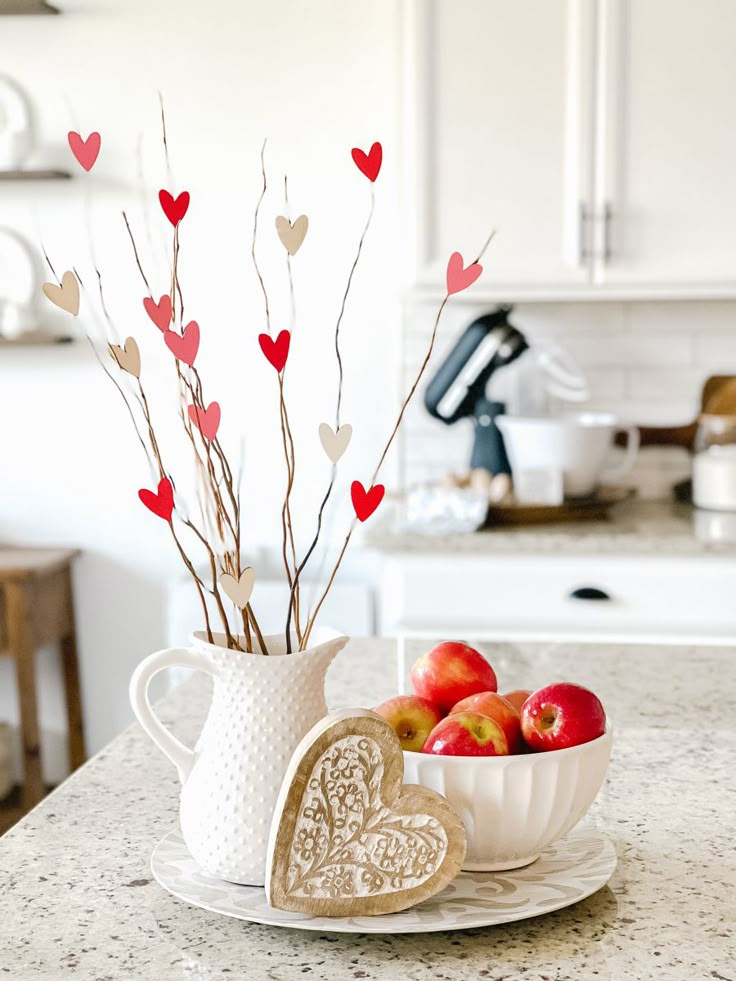 a white bowl filled with apples on top of a counter next to a cup and saucer