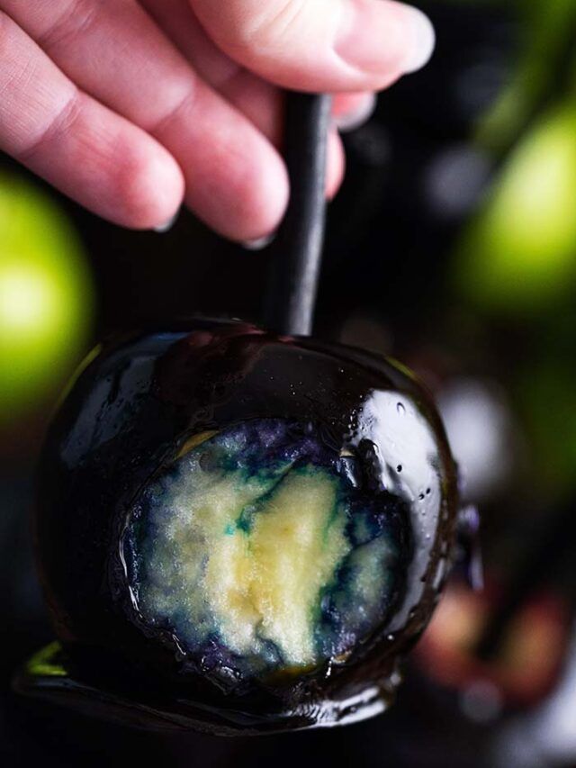 a hand holding a chocolate covered apple with blue and yellow liquid on it's surface