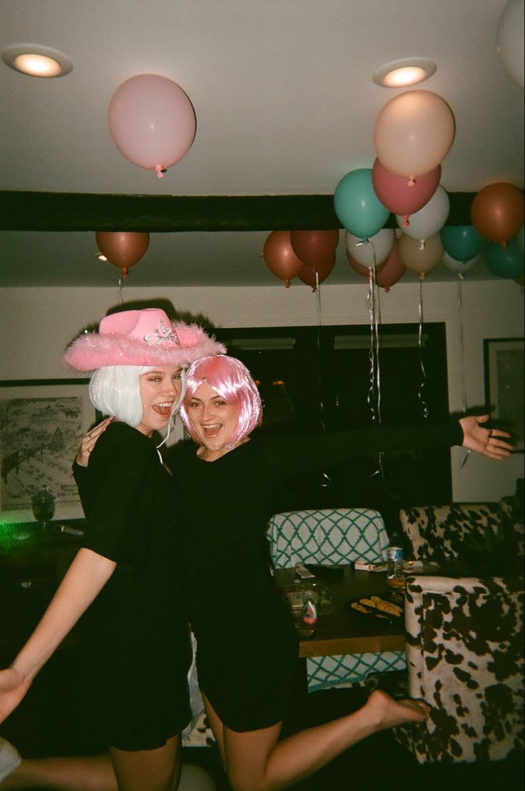 two women in black dresses and pink hats posing for the camera with balloons behind them