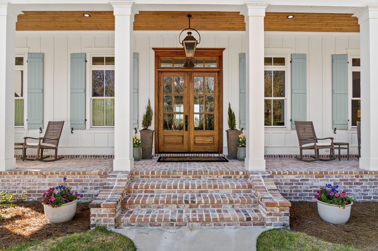 a front porch with chairs and potted plants on the steps leading up to it