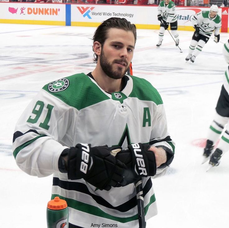 a hockey player standing on the ice with his hands in his pockets and wearing gloves