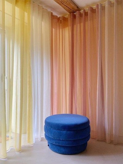 a blue ottoman sitting in front of a window with sheer curtains on the outside wall