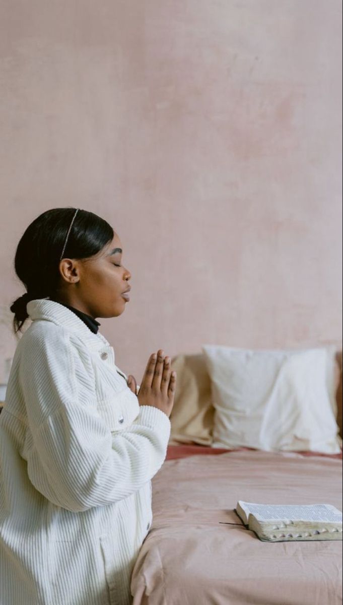 a woman sitting on a bed with her hands folded in prayer while looking off into the distance