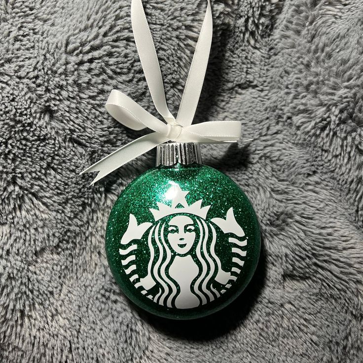 a starbucks ornament hanging from a white ribbon on a gray blanket with a bow