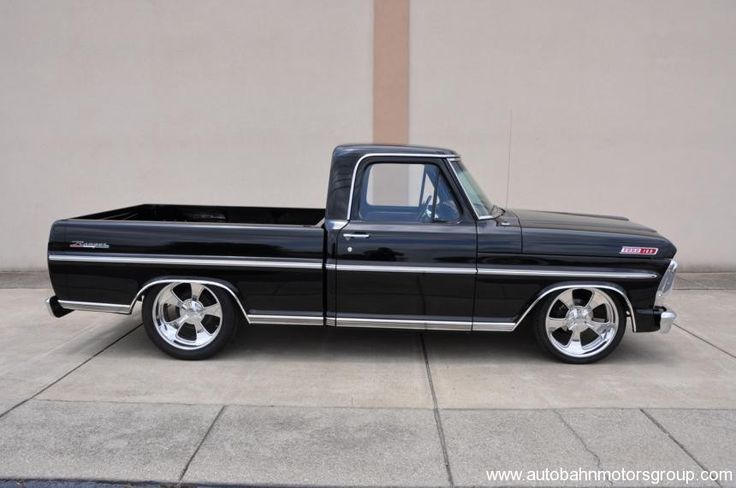 an old black truck parked in front of a building with white rims and chrome wheels