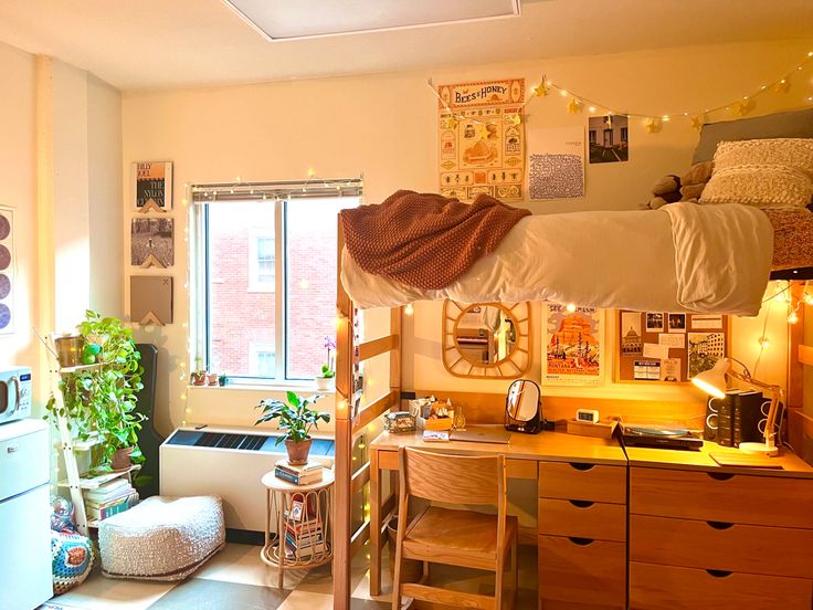 a dorm room with bunk beds, desk and window in the corner is lit by string lights