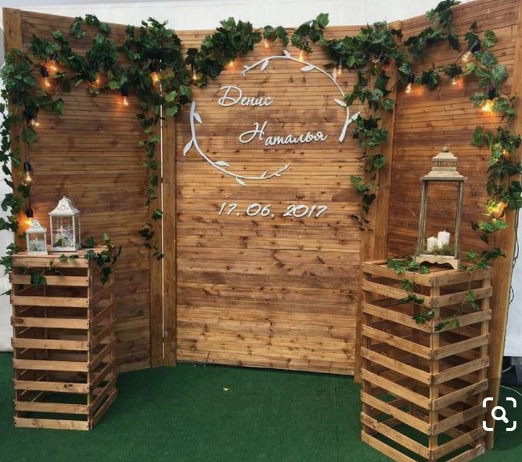 an outdoor wedding setup with greenery on the wall and wooden crates for seating in front