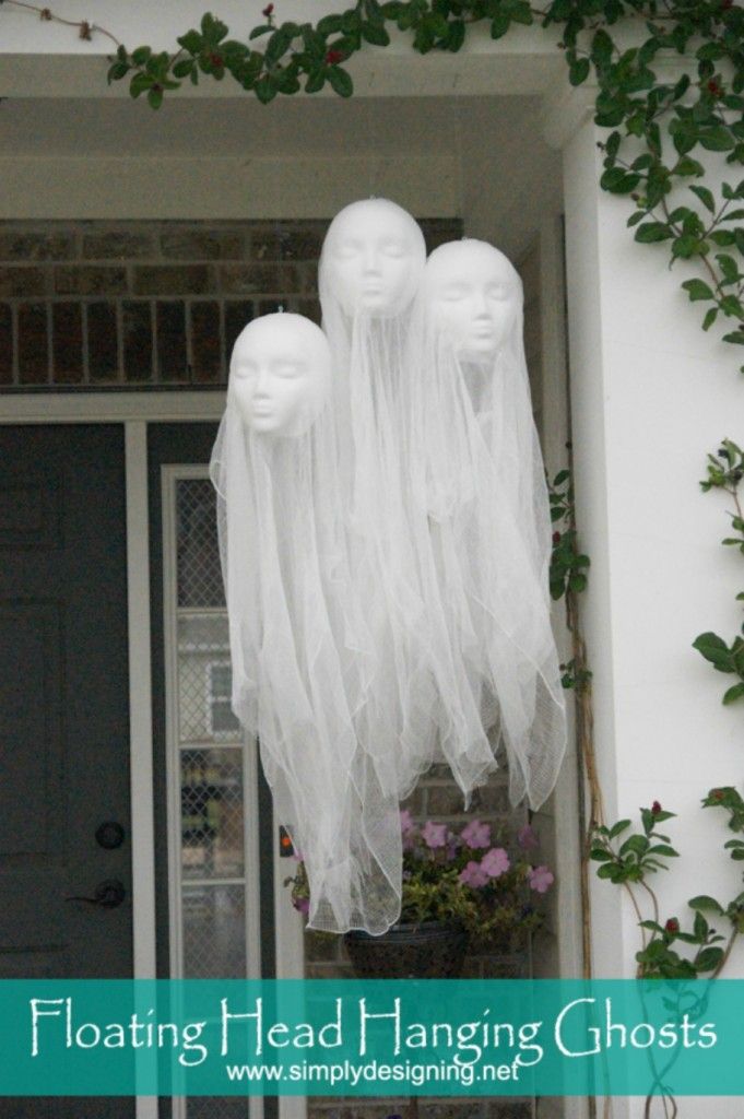 three white mannequin heads hanging from the side of a house decorated for halloween