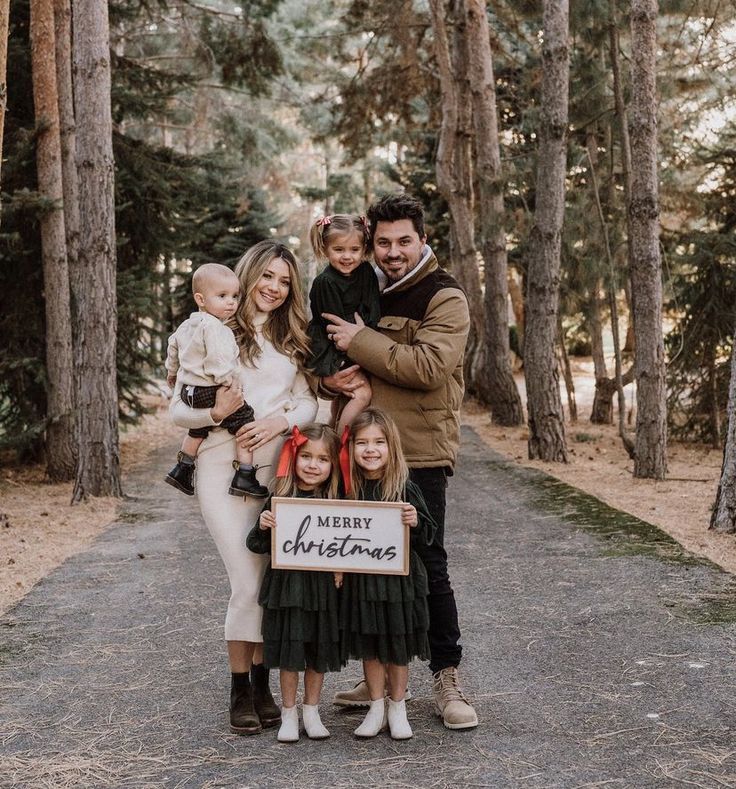 a family posing for a christmas photo in the woods with a sign that says merry christmas