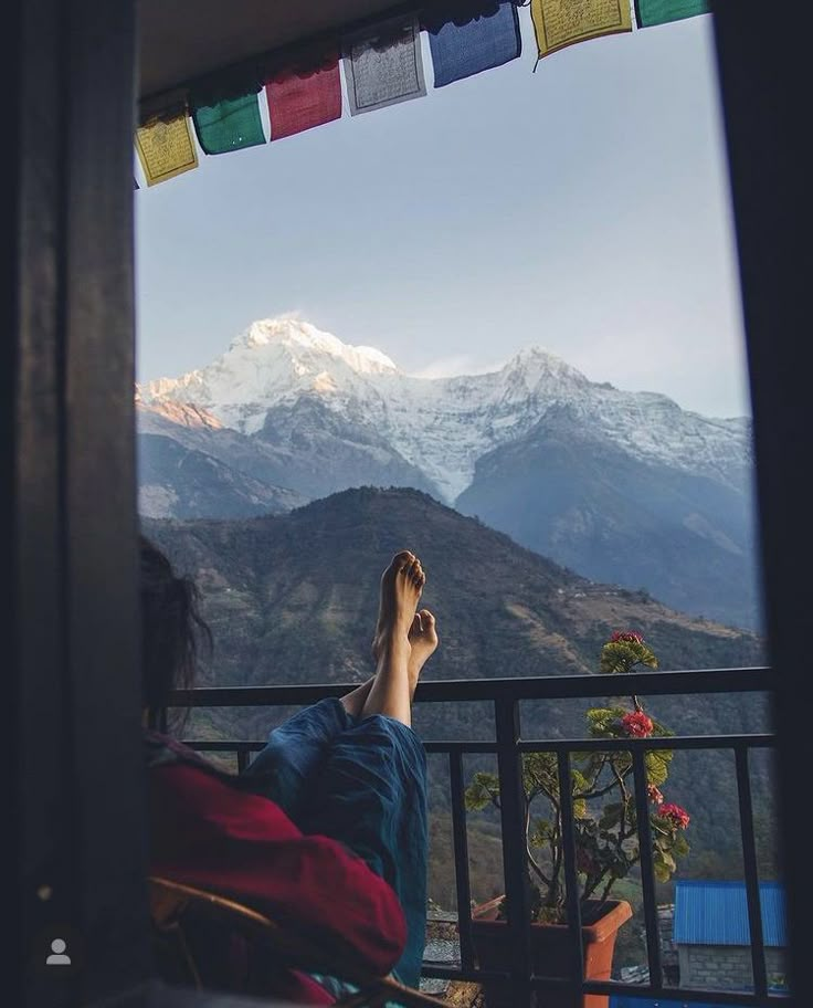 a person laying on top of a balcony next to a mountain range with their feet up in the air