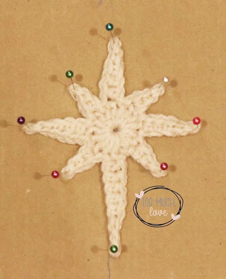 a crocheted snowflake on top of a piece of brown paper with red, green and white beads