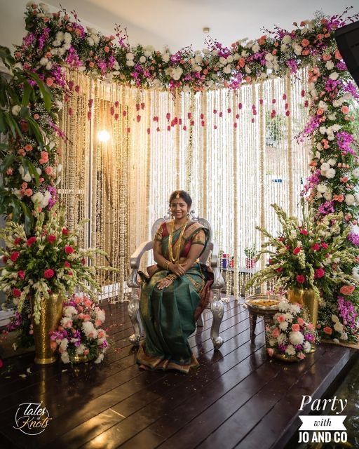 a woman sitting on a chair in front of a flower covered stage with flowers and greenery