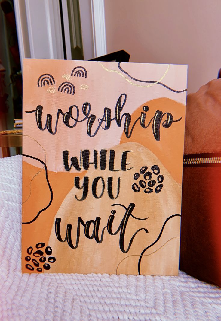 a sign that says, worship while you wait on the table next to a purse